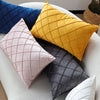 A set of three decorative velvet pillows in shades of blue, yellow, and gray on a white sofa.