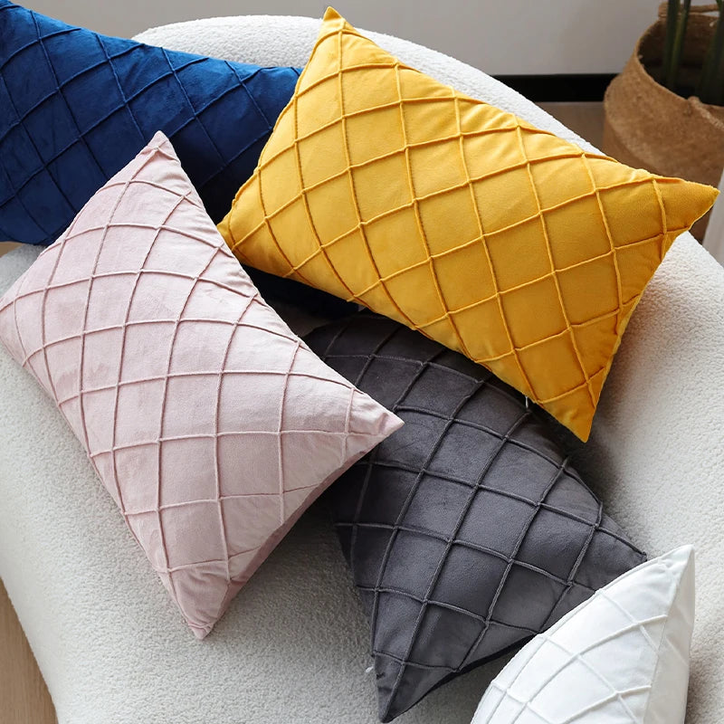 A set of three decorative velvet pillows in shades of blue, yellow, and gray on a white sofa.