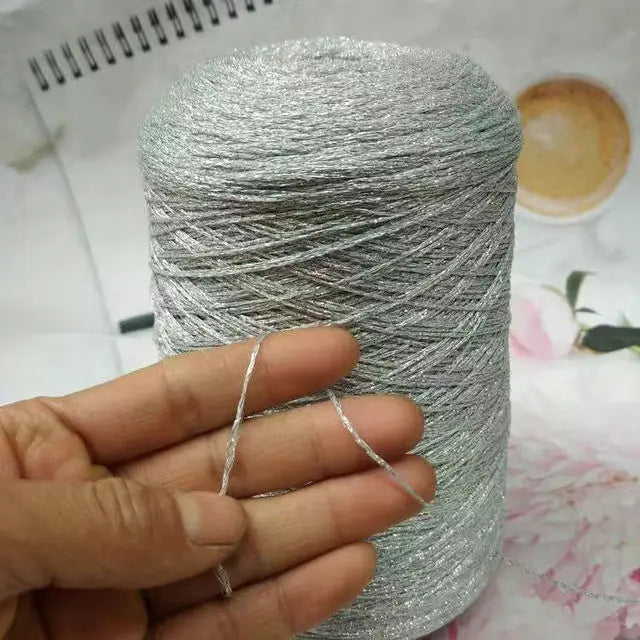 A hand holds a spool of silver glitter metallic yarn for crochet and knitting.