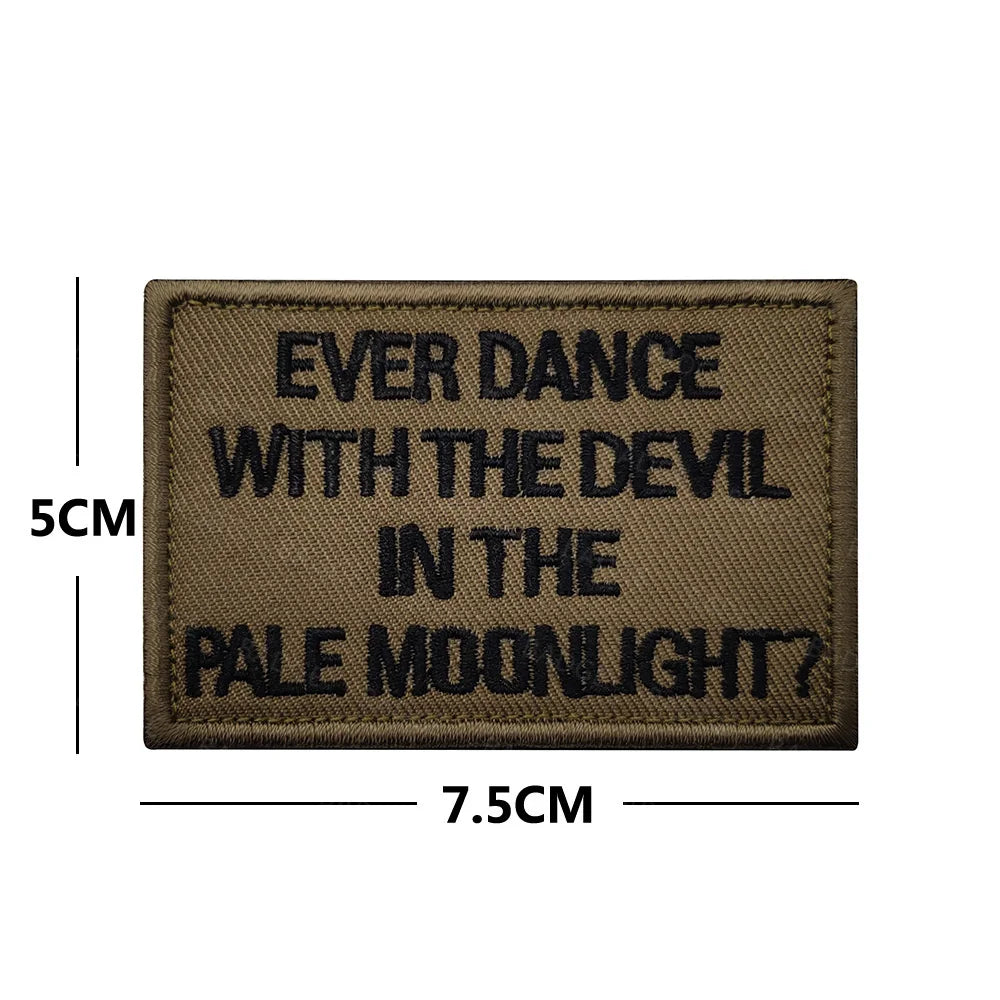 A rectangular brown embroidered patch with black text that reads Ever Dance With The Devil In The Pale Moonlight