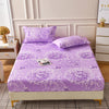 Purple floral print fitted bed sheet displayed on a white bed with light wood accents.