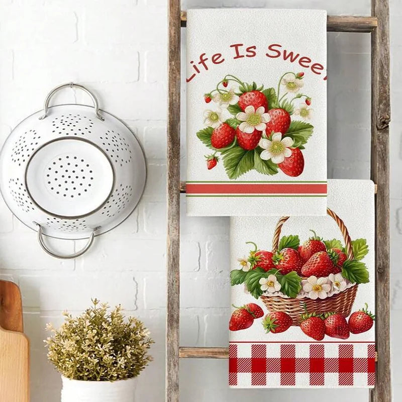 A set of two absorbent kitchen towels featuring strawberry and floral designs hanging on a wooden rack.