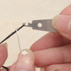 A hand holds a stainless steel sewing needle and a metal piece with a hole, demonstrating the set.