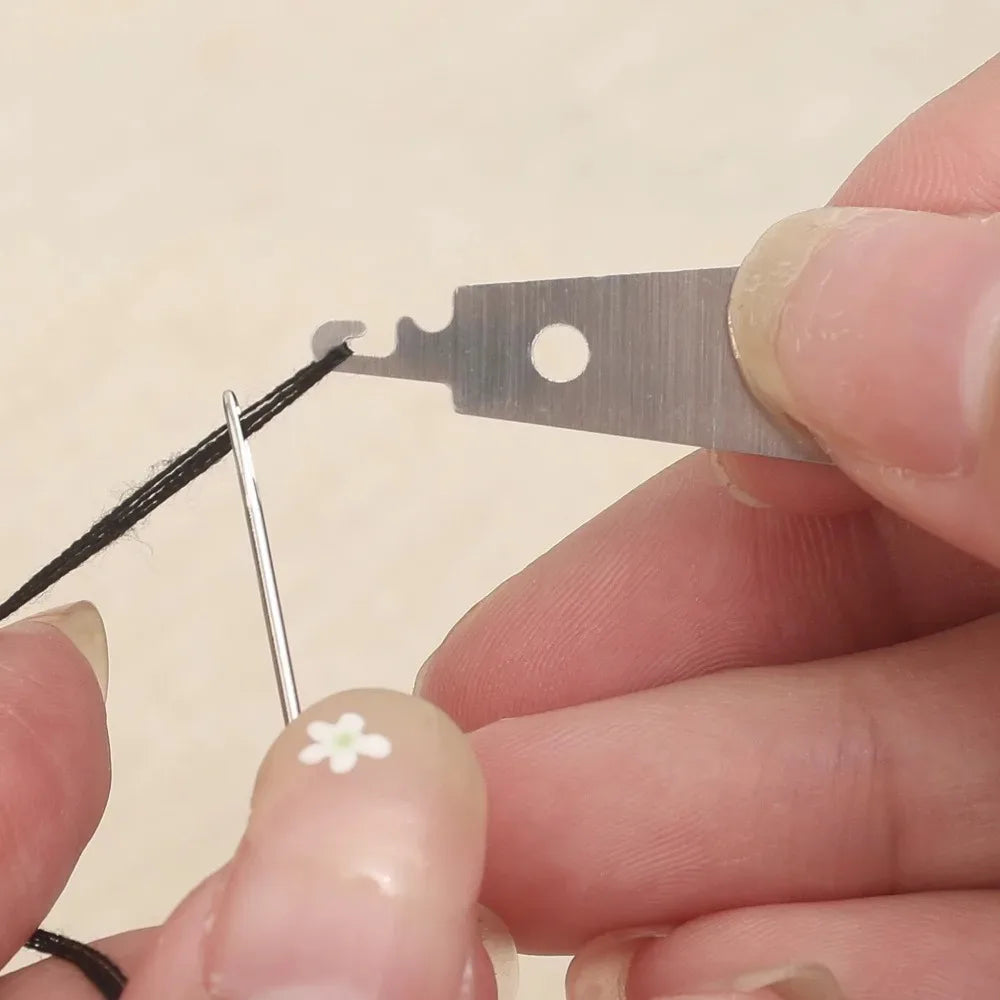 A hand holds a stainless steel sewing needle and a metal piece with a hole, demonstrating the set.