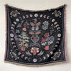 A dark throw blanket featuring geometric and bohemian patterns with various floral and crescent moon motifs.