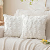 A set of two white faux fur pillow covers resting on a light-colored sofa or bed.