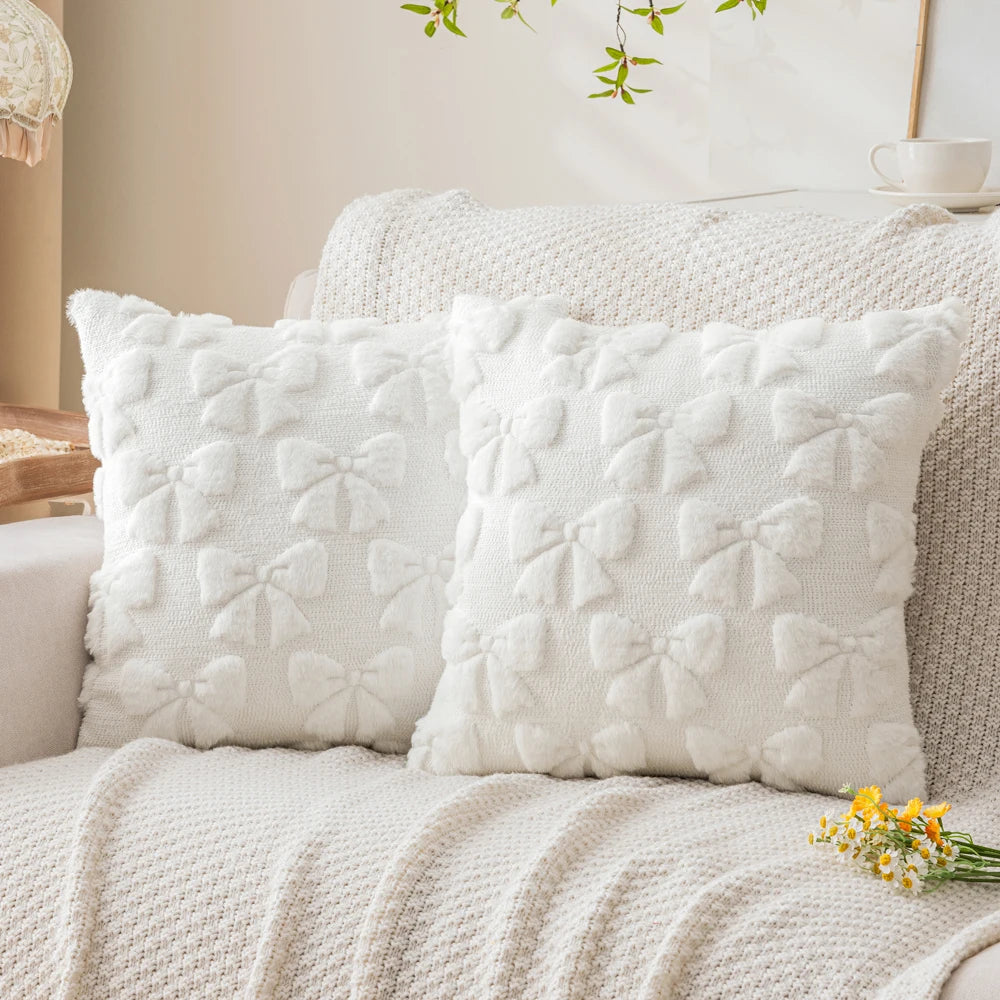 A set of two white faux fur pillow covers resting on a light-colored sofa or bed.
