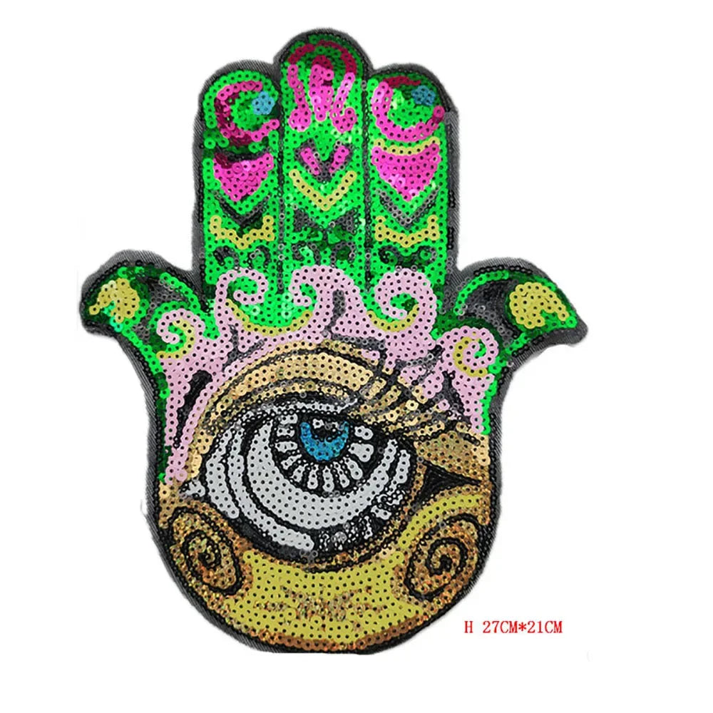 A handprint iron-on patch featuring a stylized eye design made of pink, green, and yellow sequins.