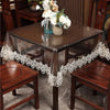 A dark wood dining table set with a lace embroidered PVC tablecloth and wooden chairs.
