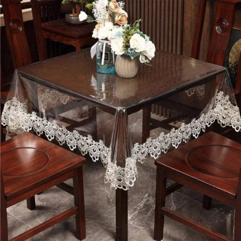 A dark wood dining table set with a lace embroidered PVC tablecloth and wooden chairs.