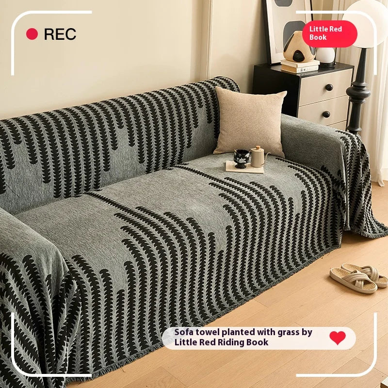 A grey sofa cover featuring a black and white herringbone pattern with tassel fringes.