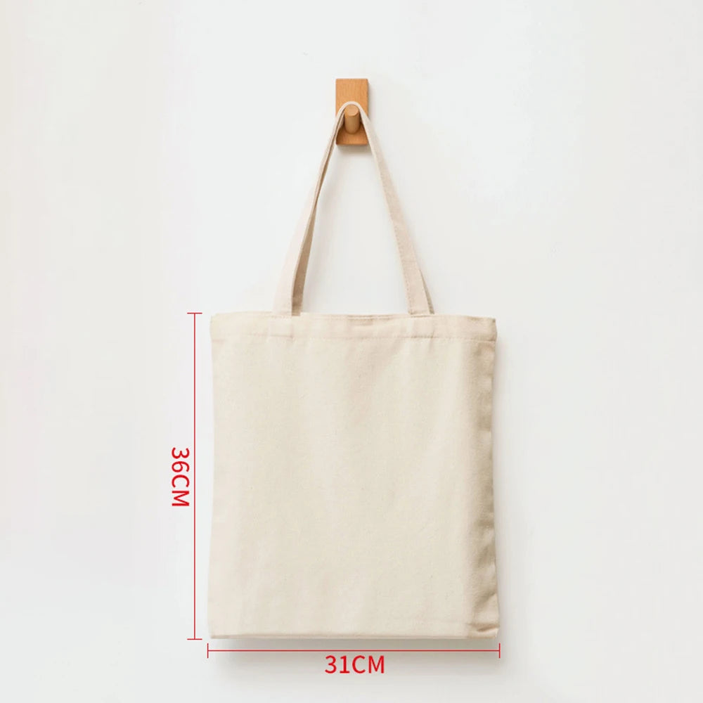 A beige reusable canvas tote bag hanging on a wooden hanger against a white background.
