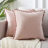 A square, dusty rose velvet cushion cover with decorative buttons rests on a light beige knitted throw.
