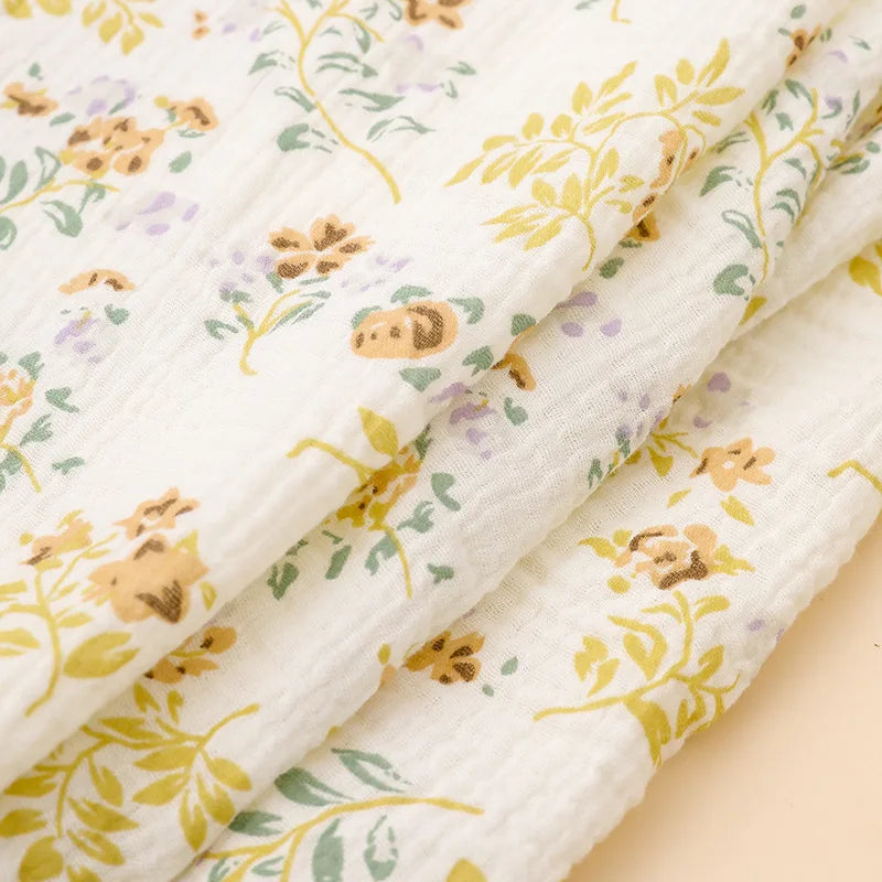 White cotton crib sheets with a delicate floral pattern featuring yellow and purple leaves.