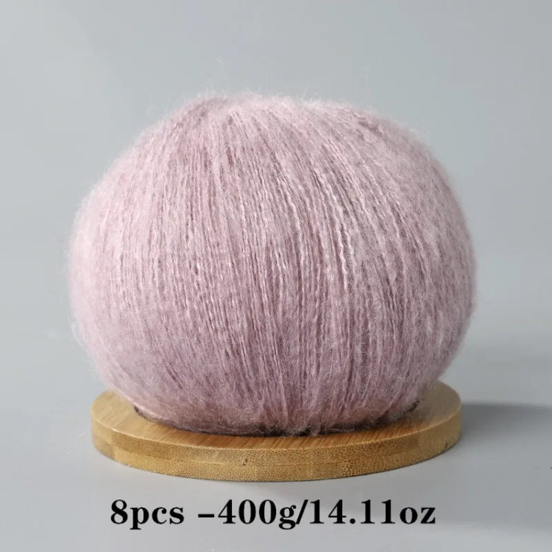 A ball of light pink mohair yarn resting on a wooden base.
