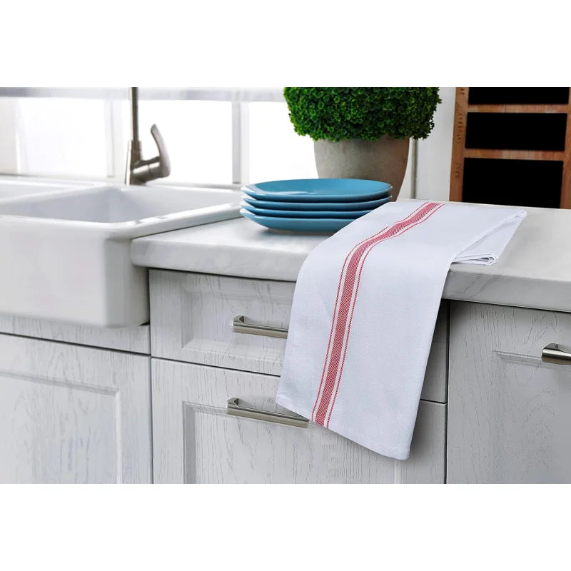 A set of white kitchen cleaning cloths with red stripes placed on a white countertop next to a sink and blue plates.