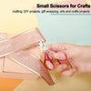 A hand holds a pair of pink precision craft scissors next to a pink gift box.