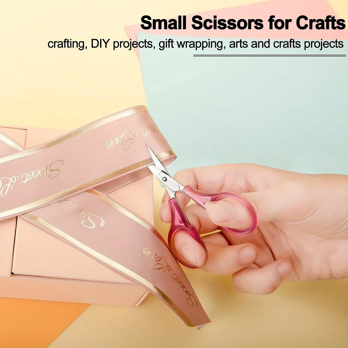 A hand holds a pair of pink precision craft scissors next to a pink gift box.