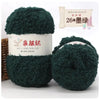 A bundle of dark green soft coral velvet yarn is shown next to its packaging and a small potted plant.