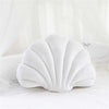 White velvet stuffed sofa cushion shaped like a decorative seashell on a white surface.