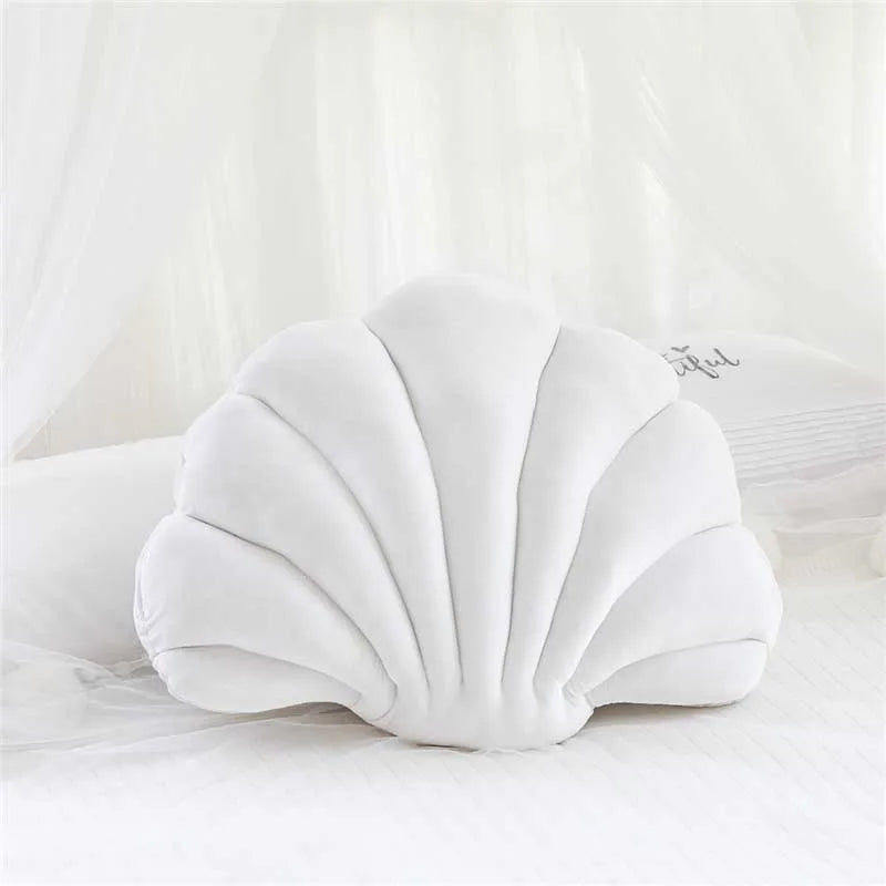 White velvet stuffed sofa cushion shaped like a decorative seashell on a white surface.