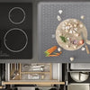 A heat-resistant silicone stove top cover mat is shown with various cooking tools and ingredients on a dark stovetop.