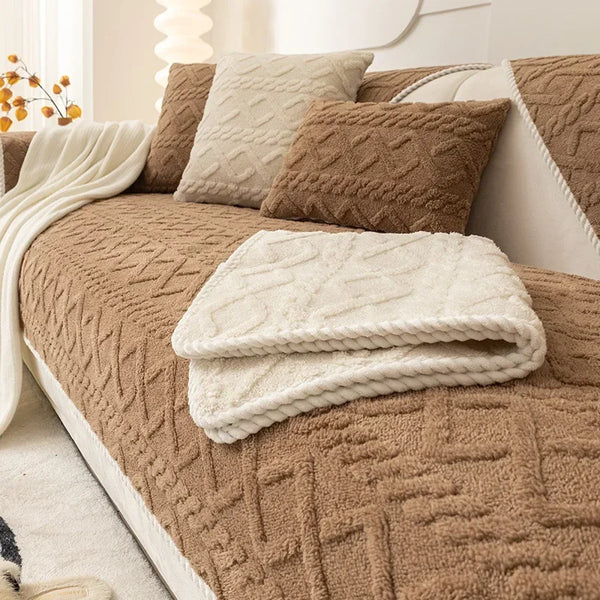 A brown textured sofa cushion cover with cream and brown throw pillows and a folded cream blanket.