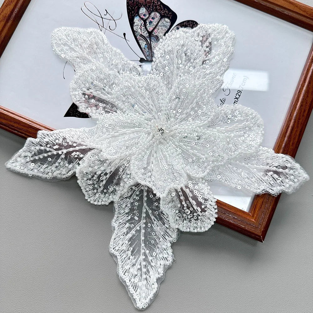 White floral applique fabric patch made of sheer lace and sequins displayed in a wooden frame.
