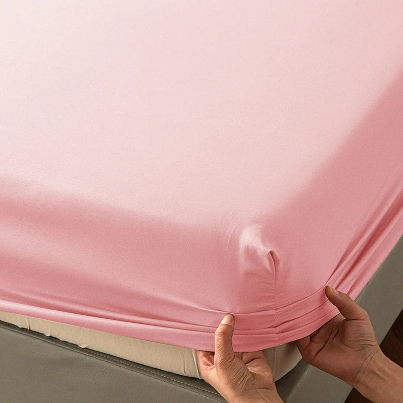 A close-up of a pink soft touch microfiber fitted sheet being held by hands.