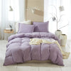 A purple quilted duvet cover set with pom-pom decoration displayed on a bed in a bright room.