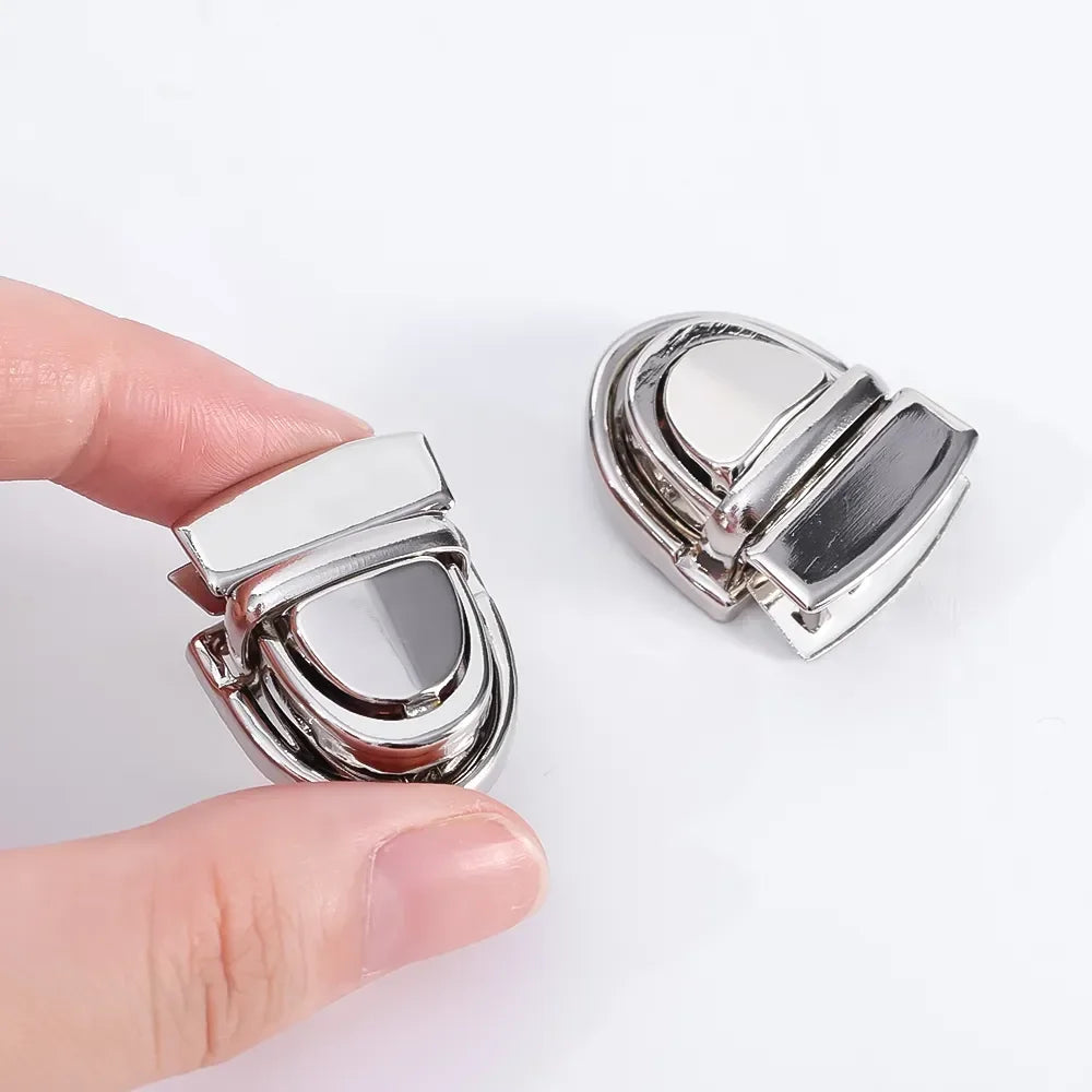 A silver metal bag clasp and buckle set being held by a hand.