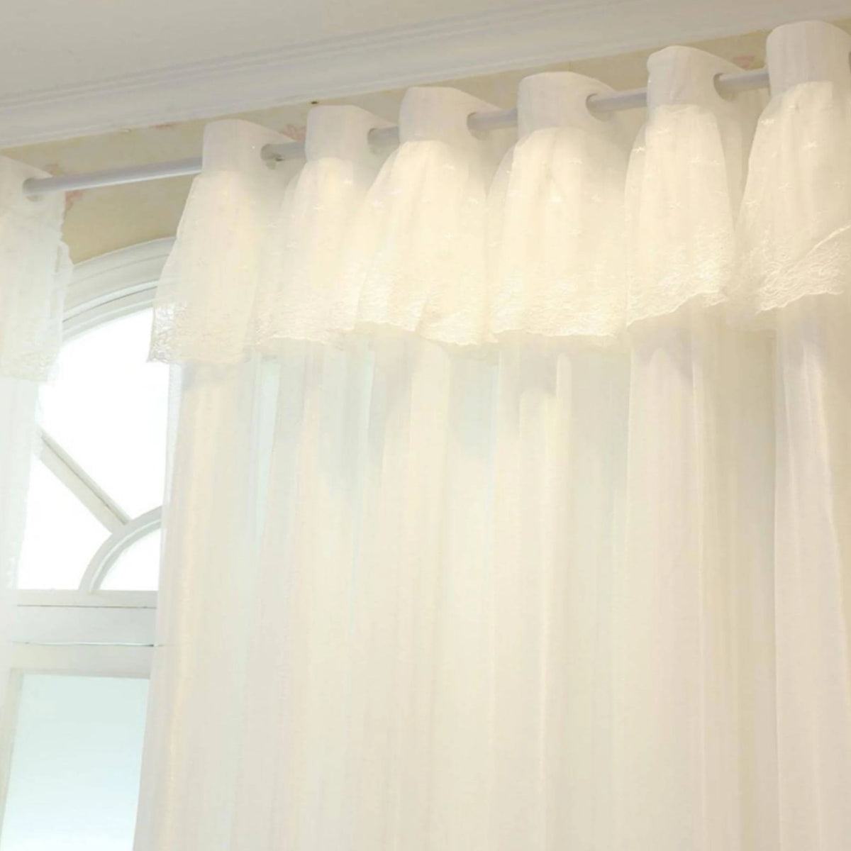 Sheer white double-layer curtains with a delicate lace overlay hanging from a rod.