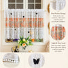 White lace cafe curtain with orange floral embroidery and butterfly applique hanging in a window.