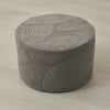 A round gray ottoman footrest slipcover featuring a woven leaf pattern.