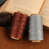 Two spools of waxed thread in copper and gray colors resting on a brown leather surface.