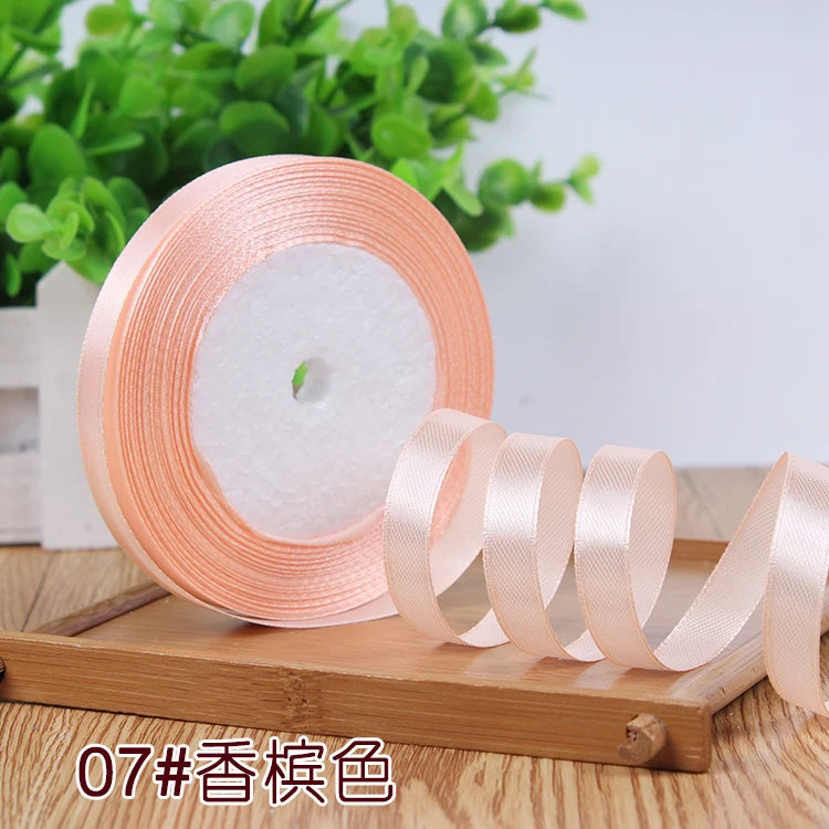 Roll of satin ribbon in a light peach color resting on a wooden surface.