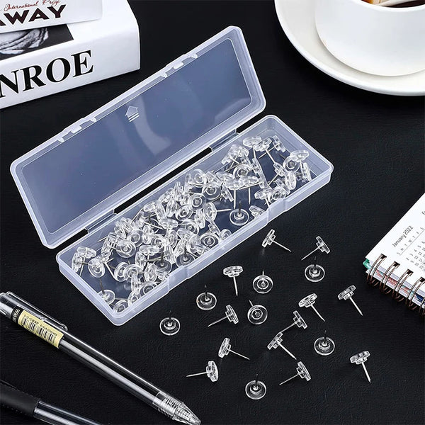 A transparent plastic box filled with round head push pins and a loose pack of similar pins on a dark surface.