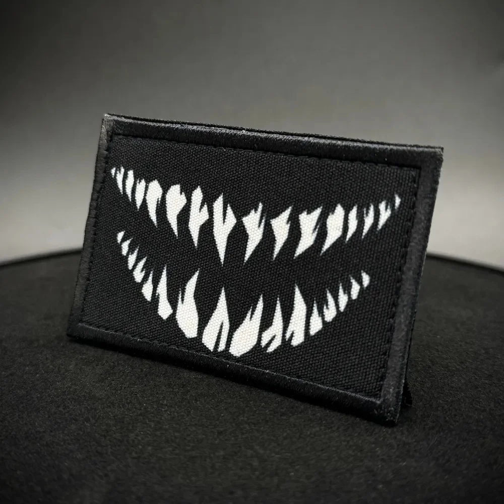 A black tactical hook and loop emblem patch featuring a white design of stylized flames.