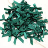A pile of dark emerald green satin ribbon bows for crafts and decor.