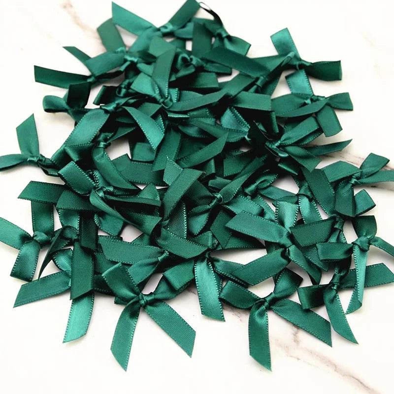 A pile of dark emerald green satin ribbon bows for crafts and decor.