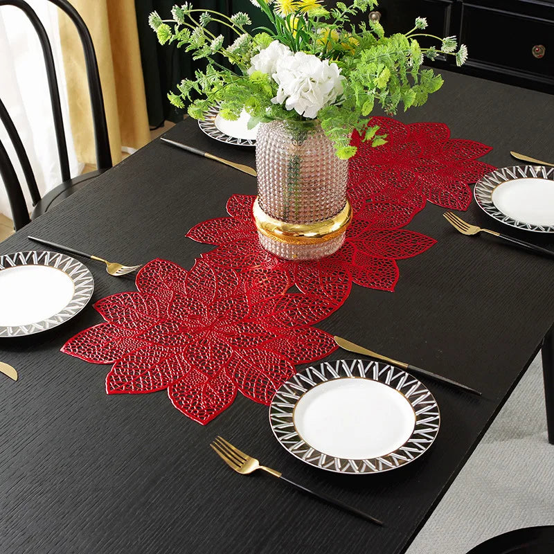 A black dining table set with red lace placemats, white plates, and gold cutlery, featuring a floral centerpiece.