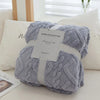 A gray plush throw blanket with a jacquard pattern is wrapped in a white box and presented on a white surface.