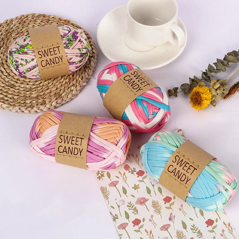 A collection of pink, blue, and yellow hand-dyed fabric strip yarn balls tied with brown labels on a white surface.