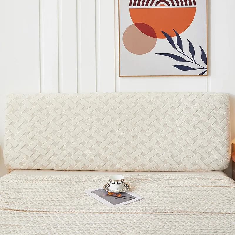 A cream quilted headboard cover on a bed with a framed abstract painting in orange and terracotta tones.