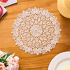 A close-up of a white floral embroidered round placemat with intricate lace detailing on a wooden table.