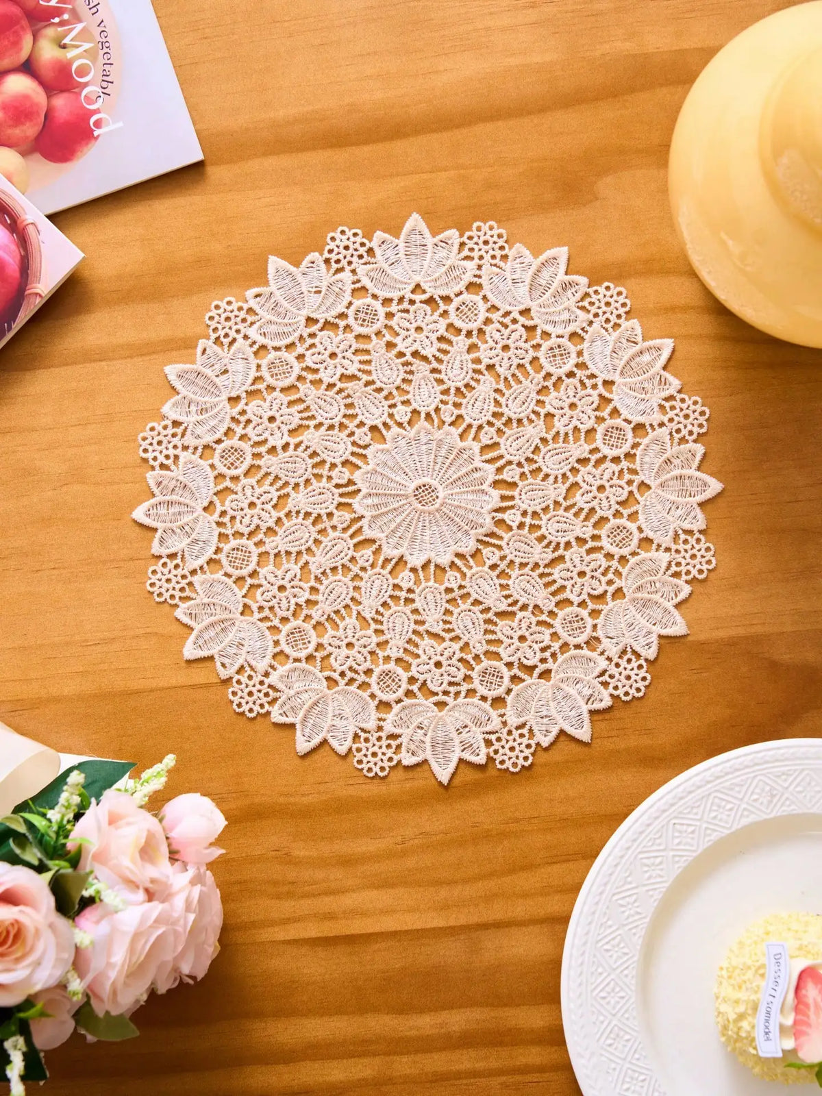A close-up of a white floral embroidered round placemat with intricate lace detailing on a wooden table.