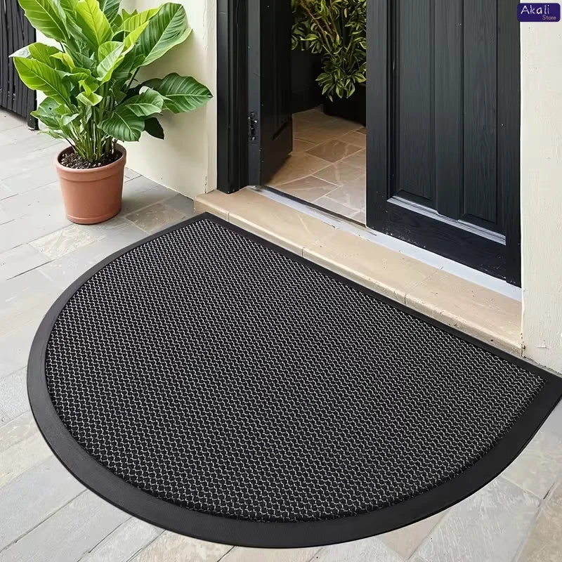 Black half-round non-slip PVC door mat placed on a light-colored tiled floor near a dark door.