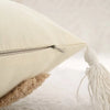 A cream-colored plush pillow cover with a gray zipper and a white tassel detail.