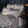 A set of silky satin pillow covers in gray and off-white are displayed on a bed.