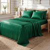 A dark emerald green satin bedding set with striped duvet and pillows on a wooden bed.